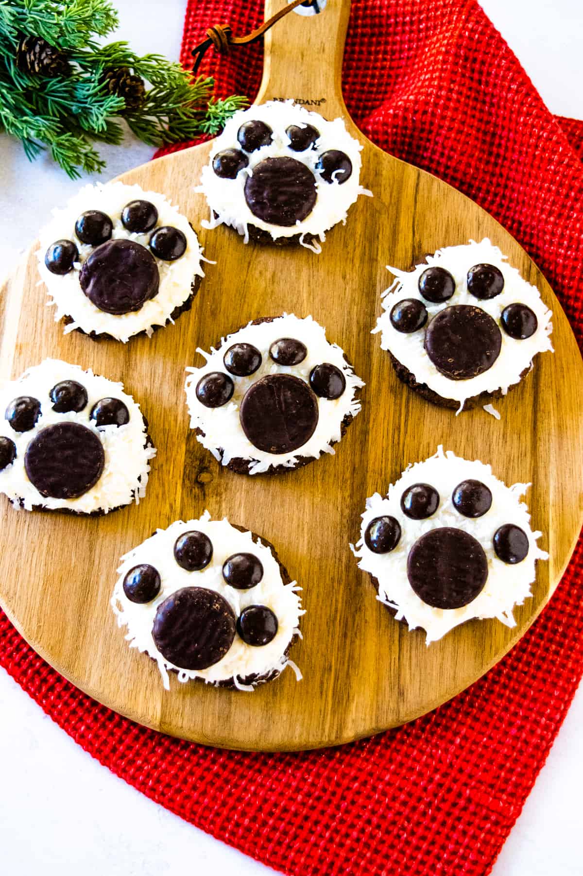 Upclose image of Polar Bear Paw Cookies on a wooden tray with evergreen and red cloth tablescape.