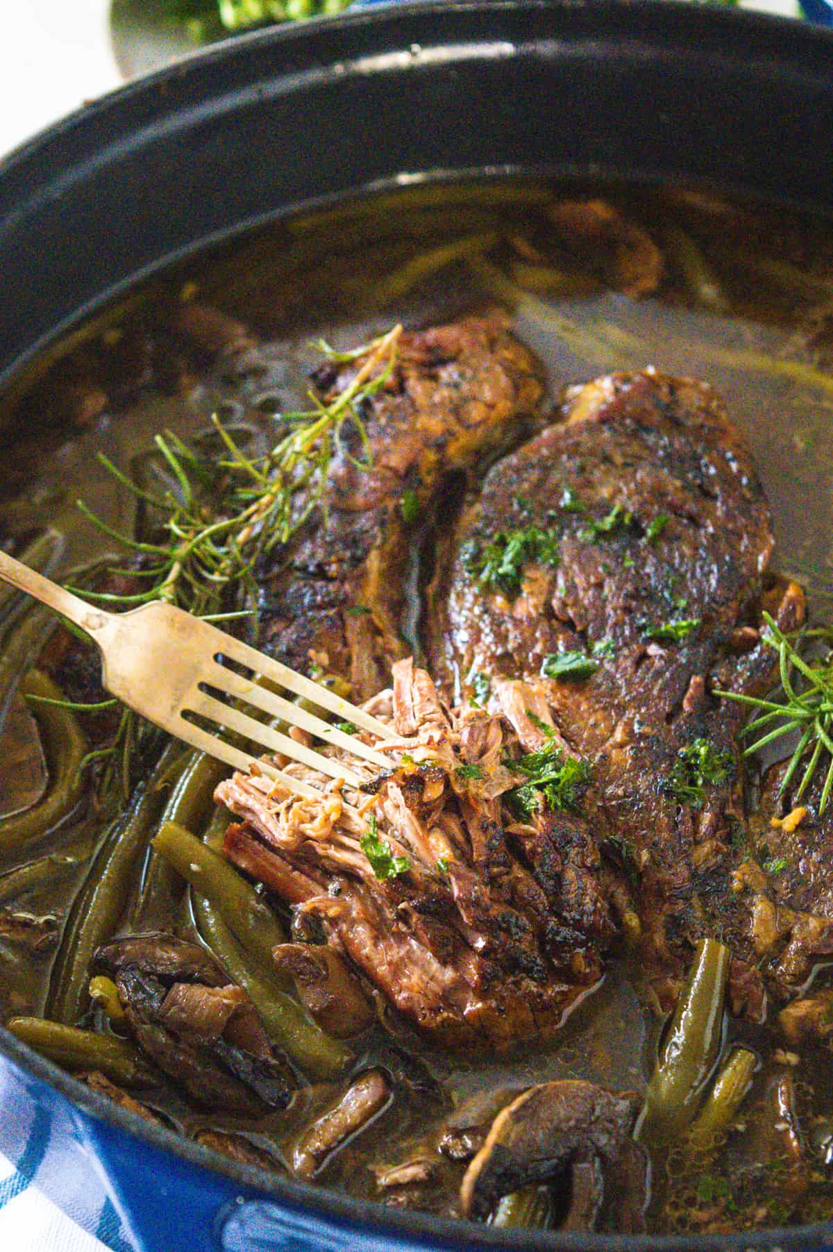 Pot roast in a dutch oven with green beans and mushrooms served with a fork.