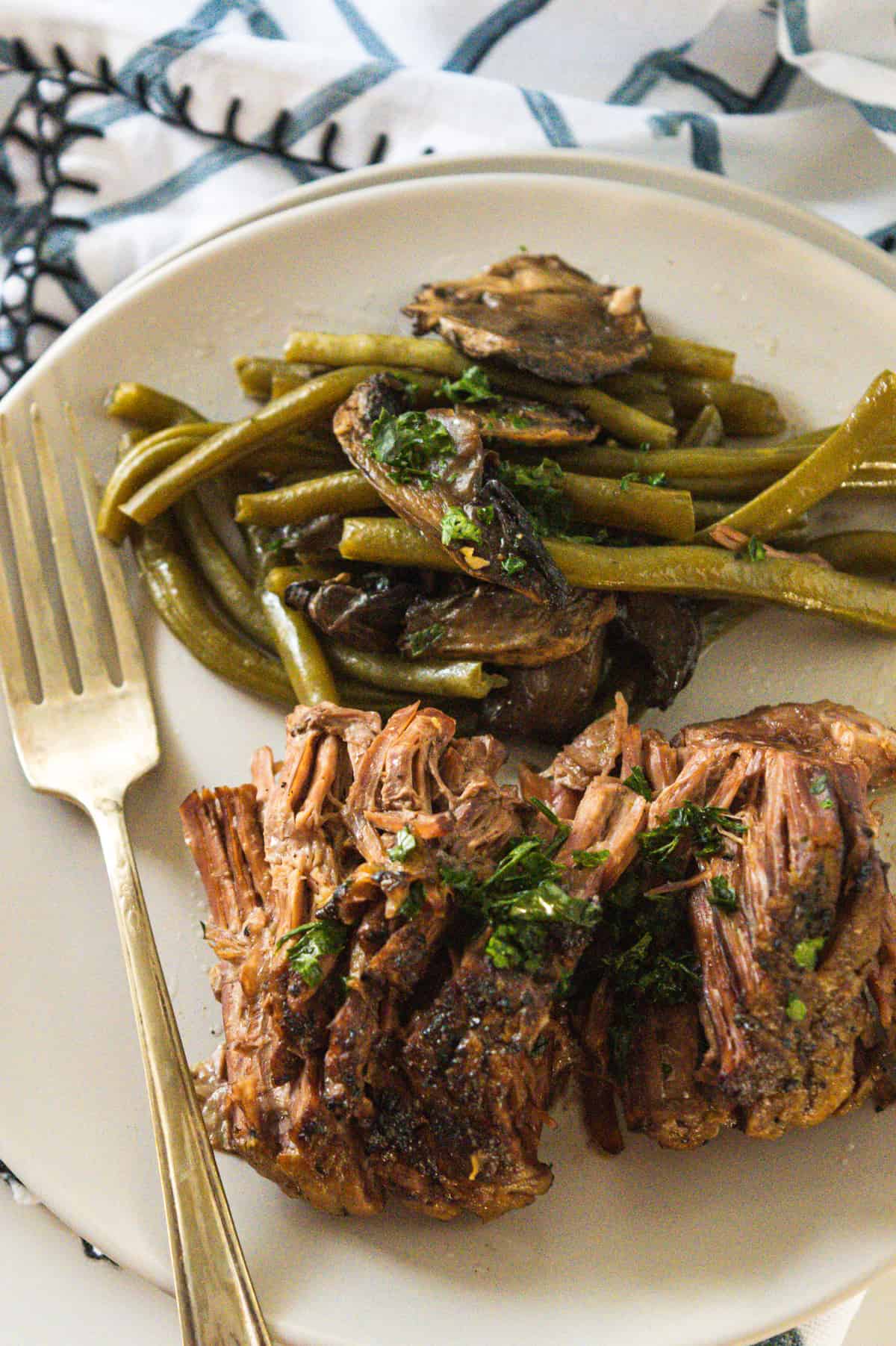 Pot roast with green beans and mushrooms served on an off-white plate.