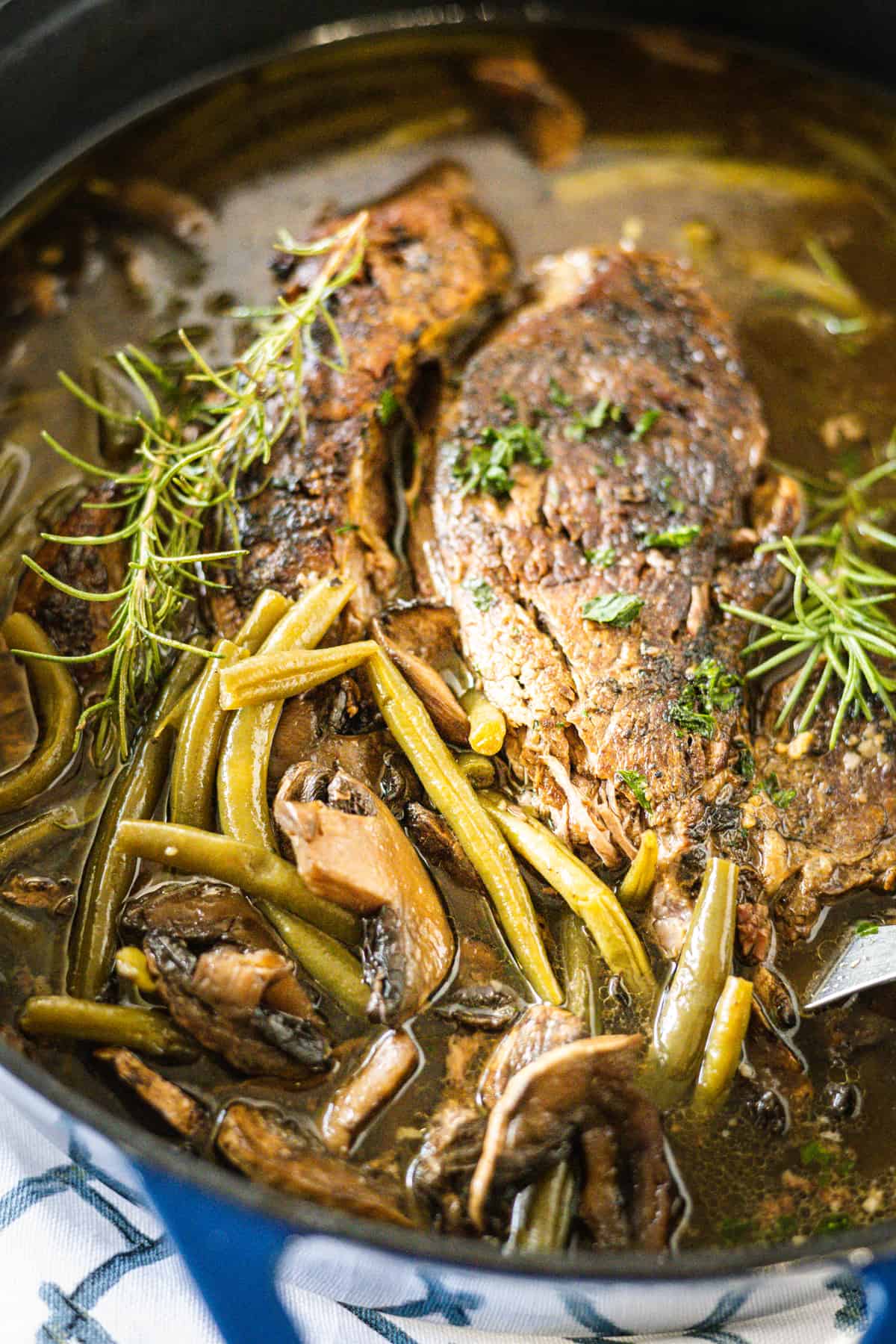 Up close image of a pot roast cooked with green beans and mushrooms.