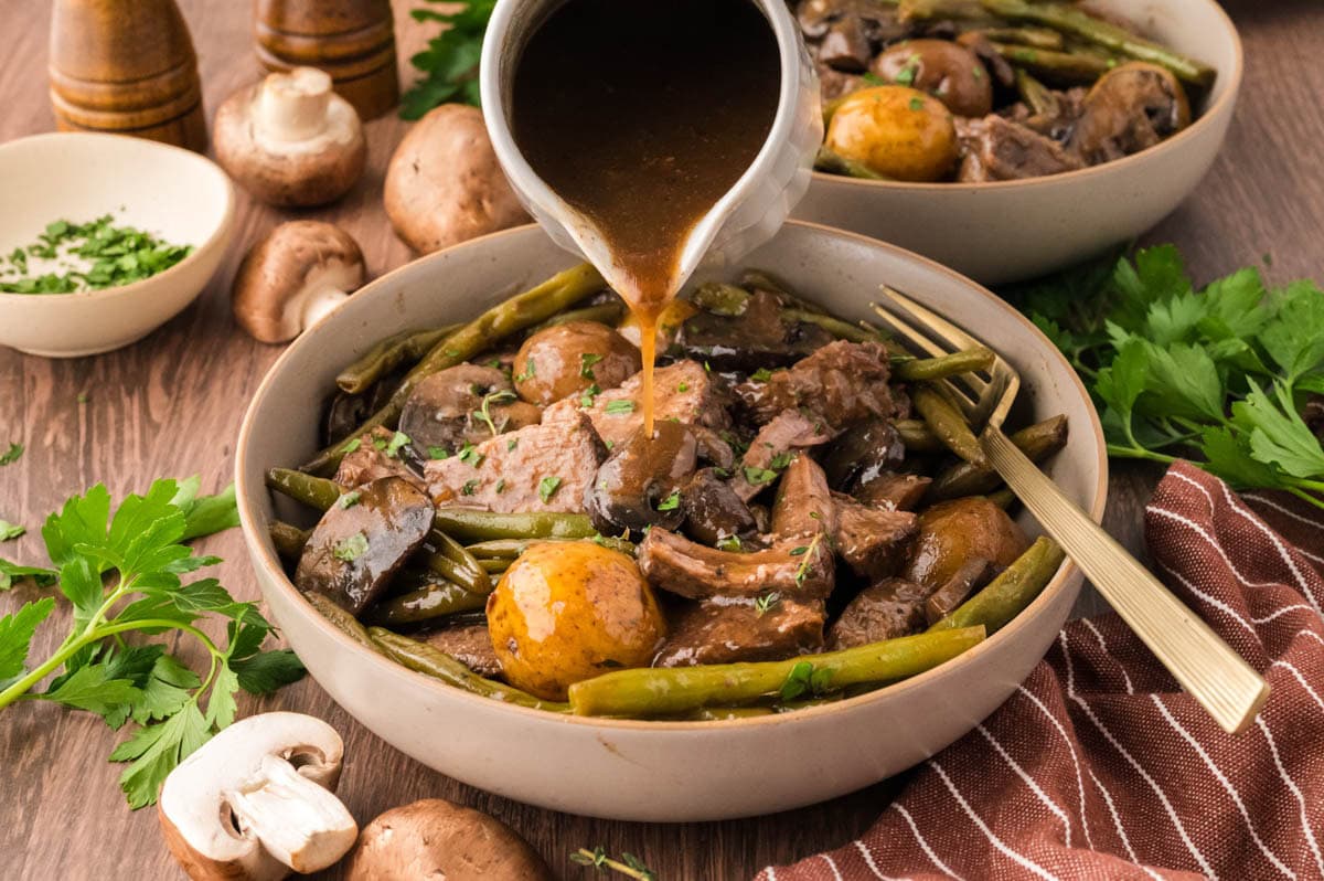Pouring gravy over the plated roast with green beans, potatoes, and mushrooms.