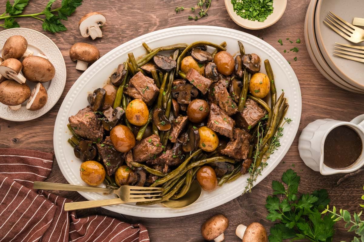 A pot roast with vegetables on a white serving plate set on a dark wood table.