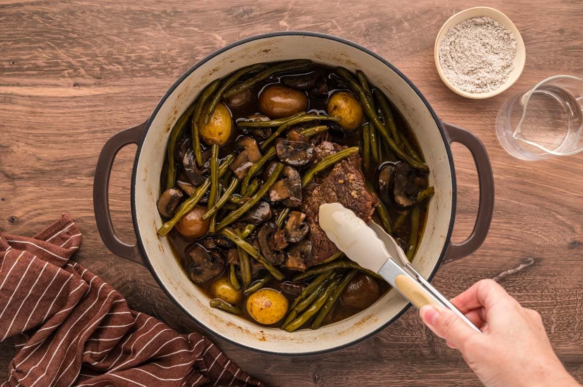 Removing roast and vegetables with tongs from the dutch oven to make the gravy.
