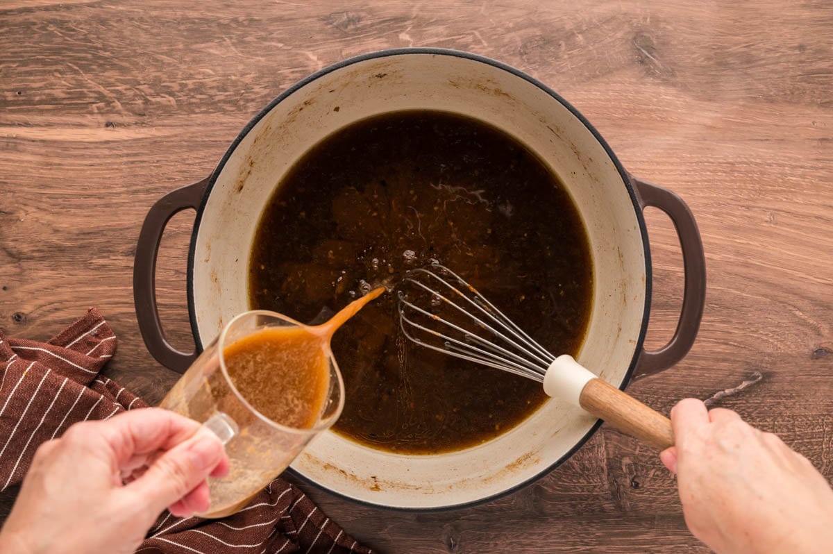Pouring in gravy mix while whisking in braising liquids in dutch oven.