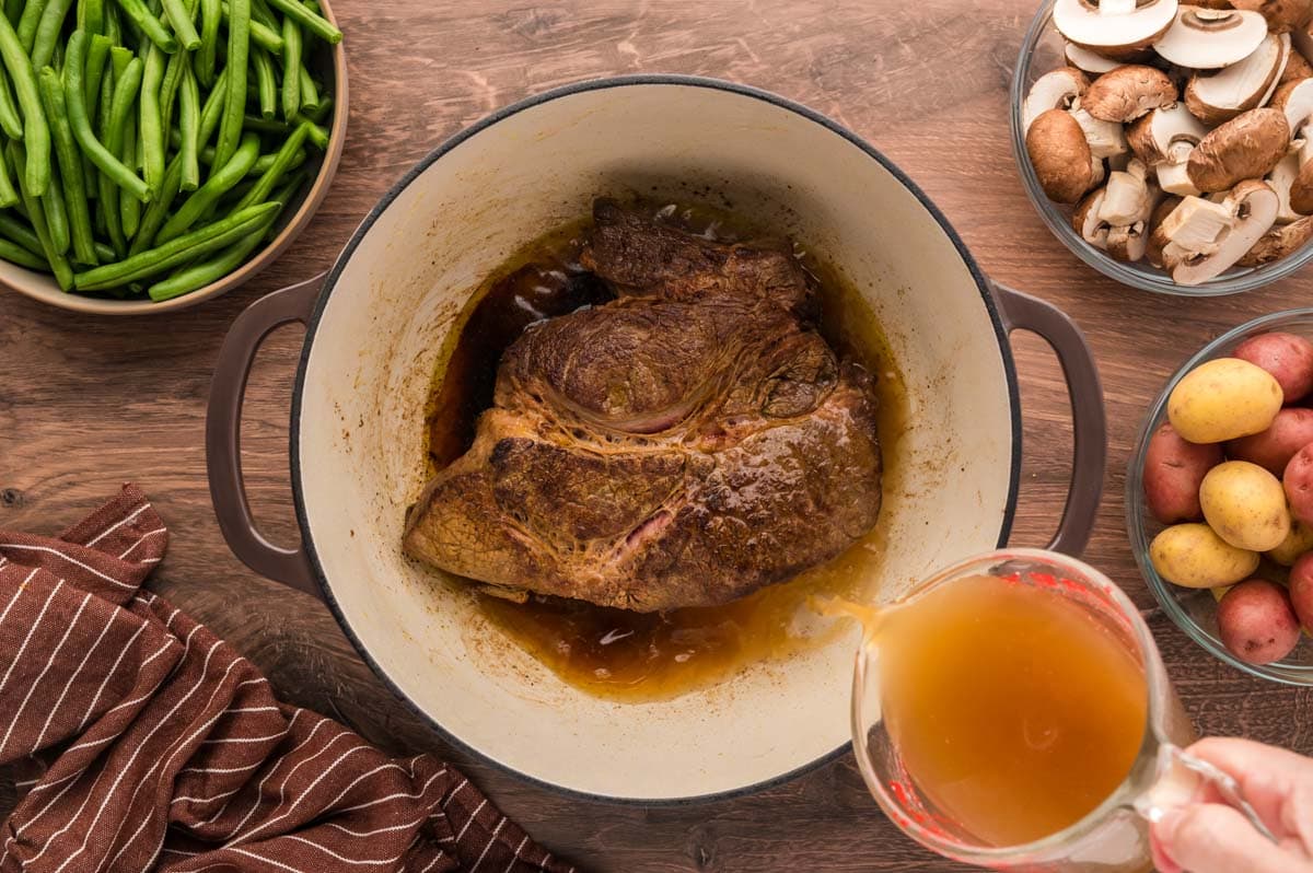Pouring beef broth into the dutch oven with the seared roast.