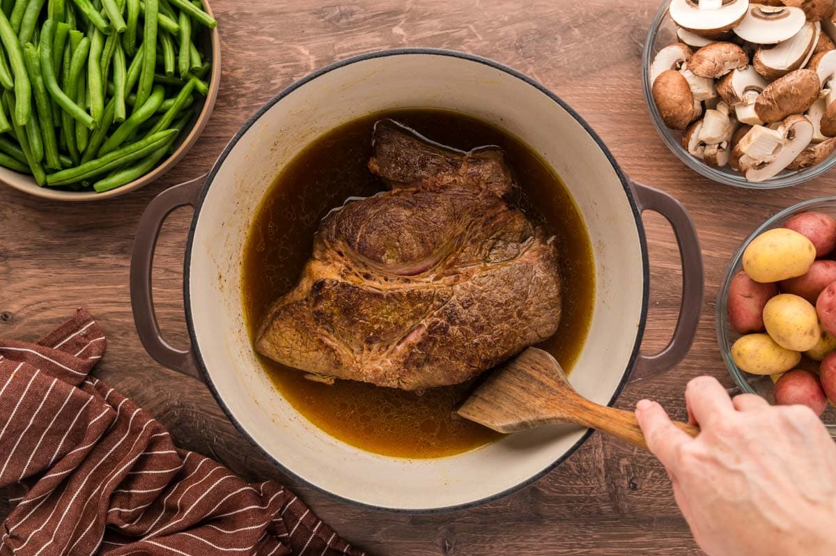 Using a wood spatula to scrape up drippings on bottom of dutch oven after searing roast.