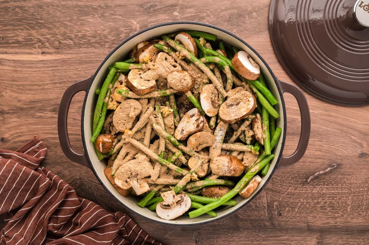 Green beans, potatoes and mushrooms added to the dutch oven over the seared roast the sprinkled with seasoning, garlic and au jus mix.