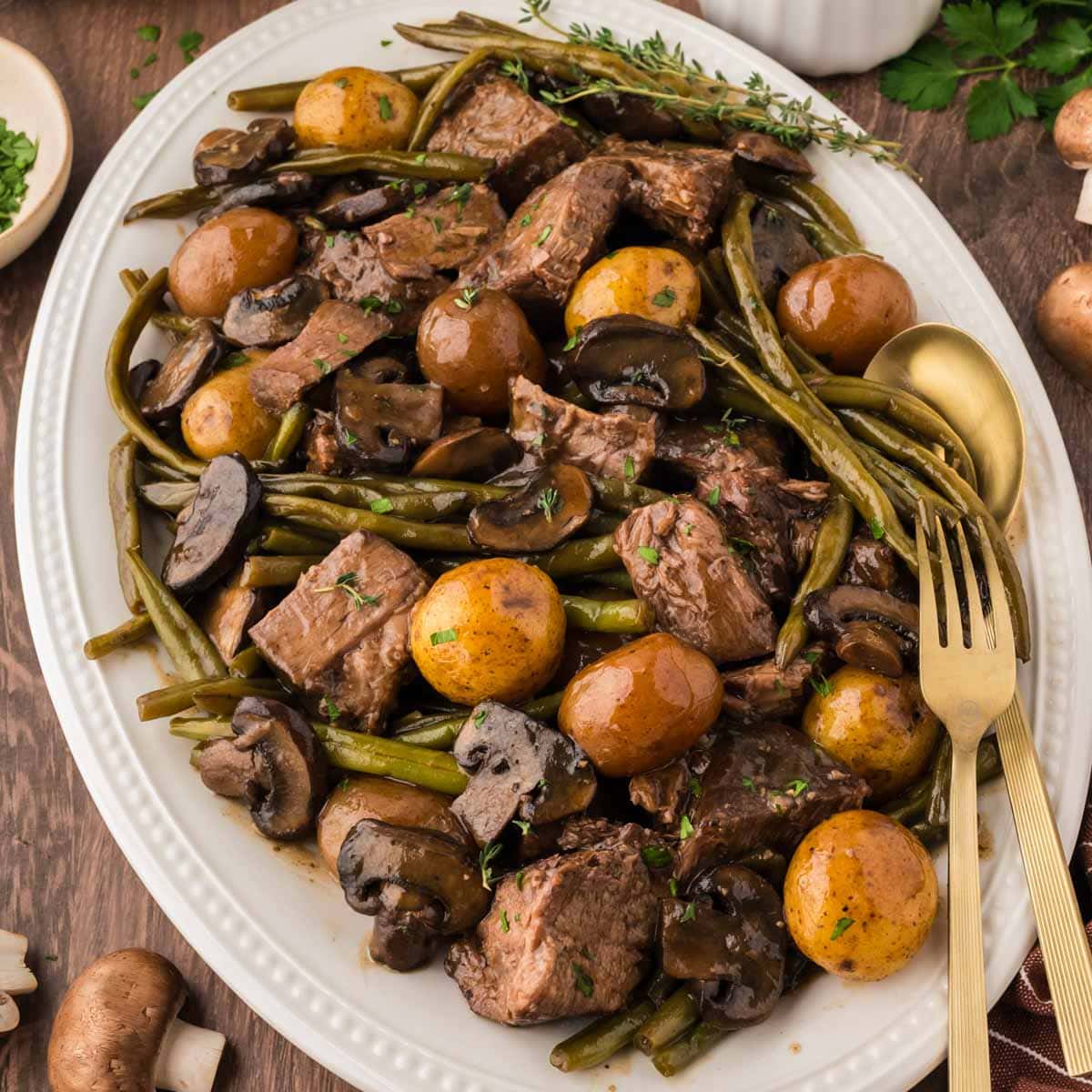A sliced pot roast with green beans, mushrooms, potatoes and gravy on a white serving platter.