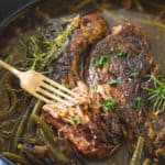 Upclose image of pot roast surrounded by green beans and mushrooms in a beef broth.