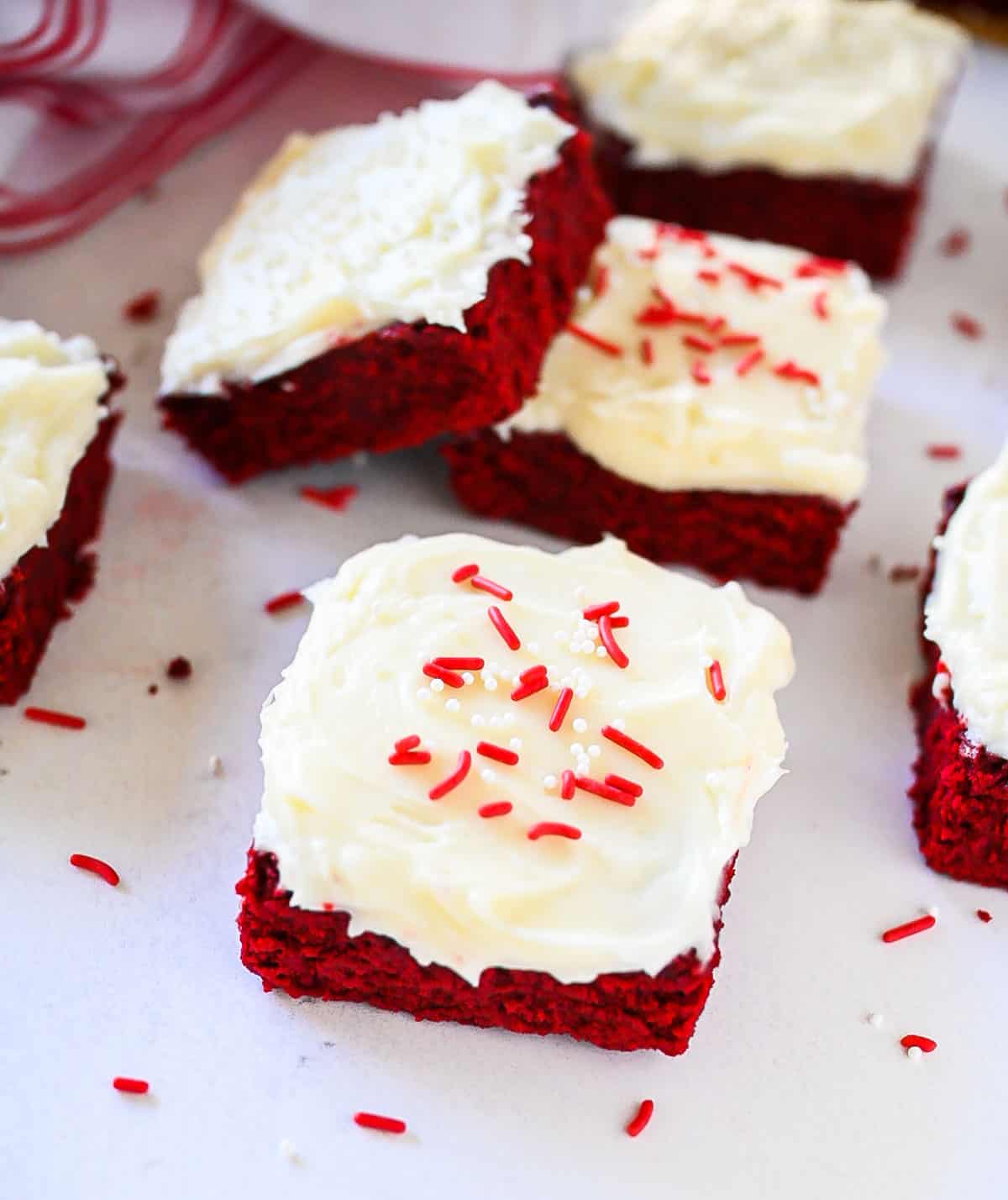 Sliced red velvet brownies with icing and sprinkles on a white tray.