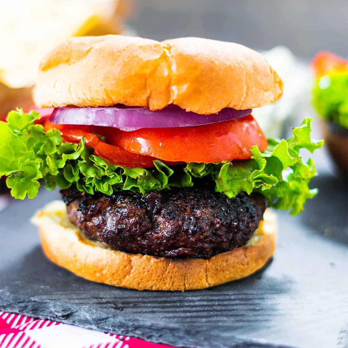 Burger stuffed with bacon and cheddar on a bun with lettuce, tomato, and onion.