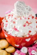 Valentines Day Dip Pinterest image of dip in a red heart bowl with a little debbie heart snack cake on top.