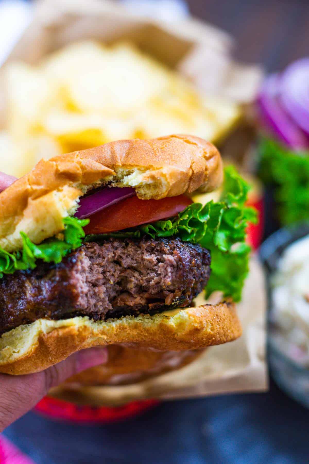 Upclose image of a bite taken out of bacon cheeseburger on a bun with all the fixings.