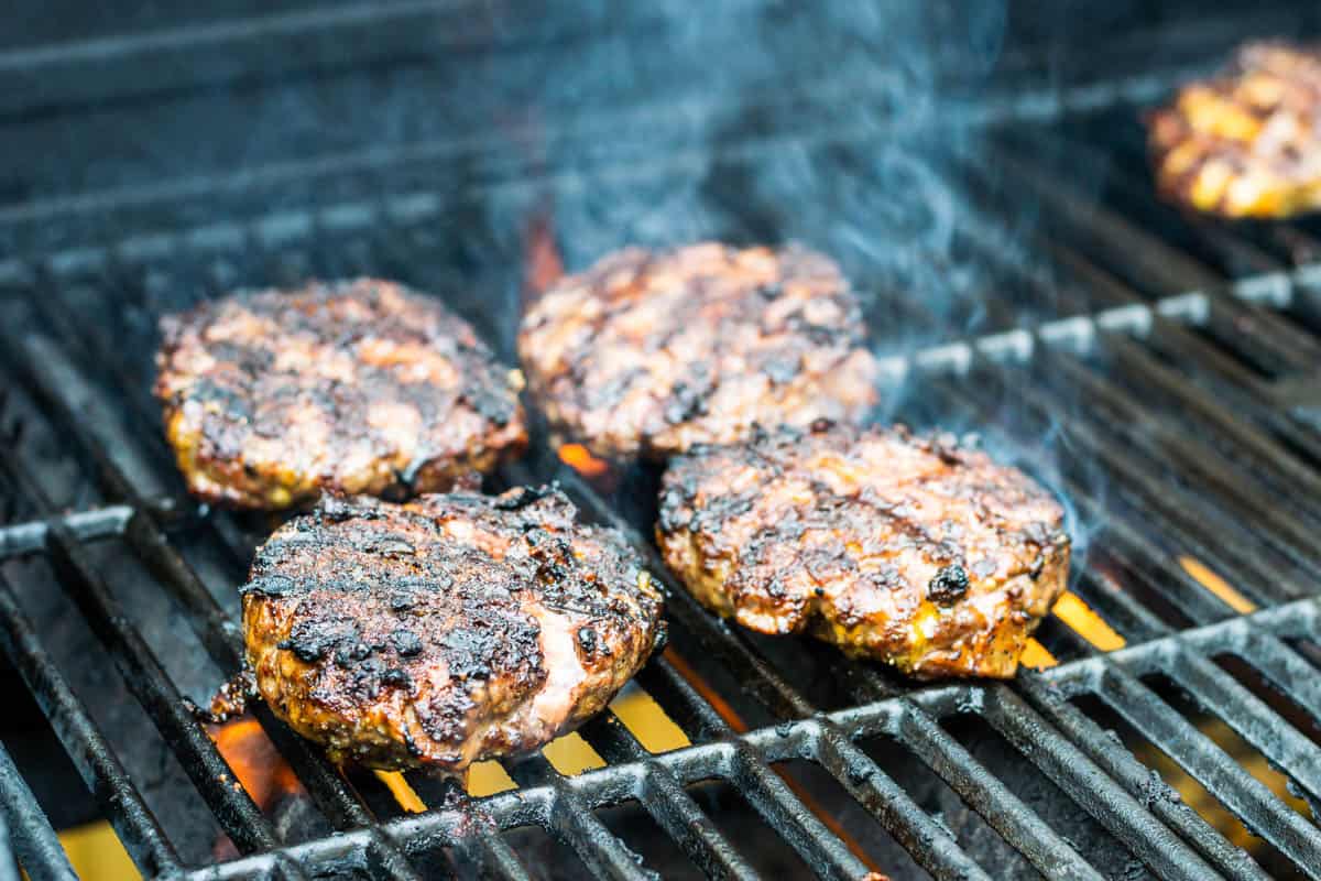 Bacon Cheddar Cheese Burgers on the grill with grill flames underneath while they are cooking