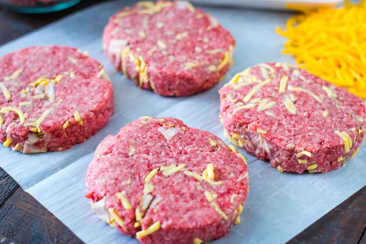 Ground chuck mixed with cheddar cheese and bacon pieces pattied out and sitting on a piece white parchment paper.