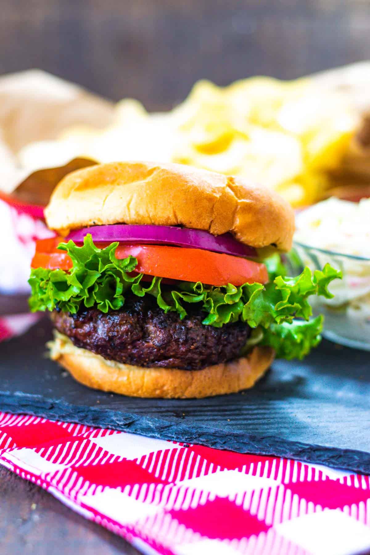 A stuffed bacon cheddar burger on a bun with lettuce, tomato and red onion.