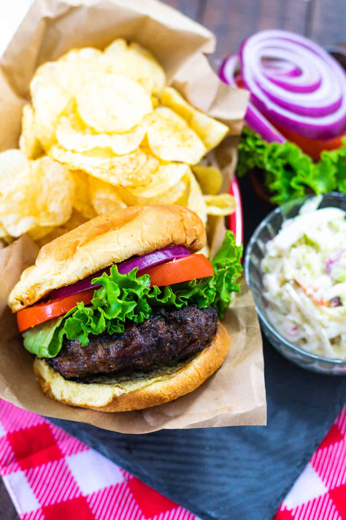 Upclose image of a stuffed bacon cheddar cheeseburger on a slate platter served with chips and slaw.