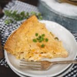 Flaky chicken pot pie slice on a speckled grey plate with a fork set in front of pie.