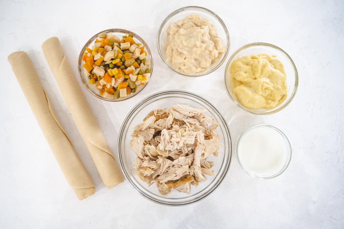 Image of chicken pot pie ingredients - two premade pie crust, veg-all vegetables, shredded chicken, cream of chicken and potato soups, milk.