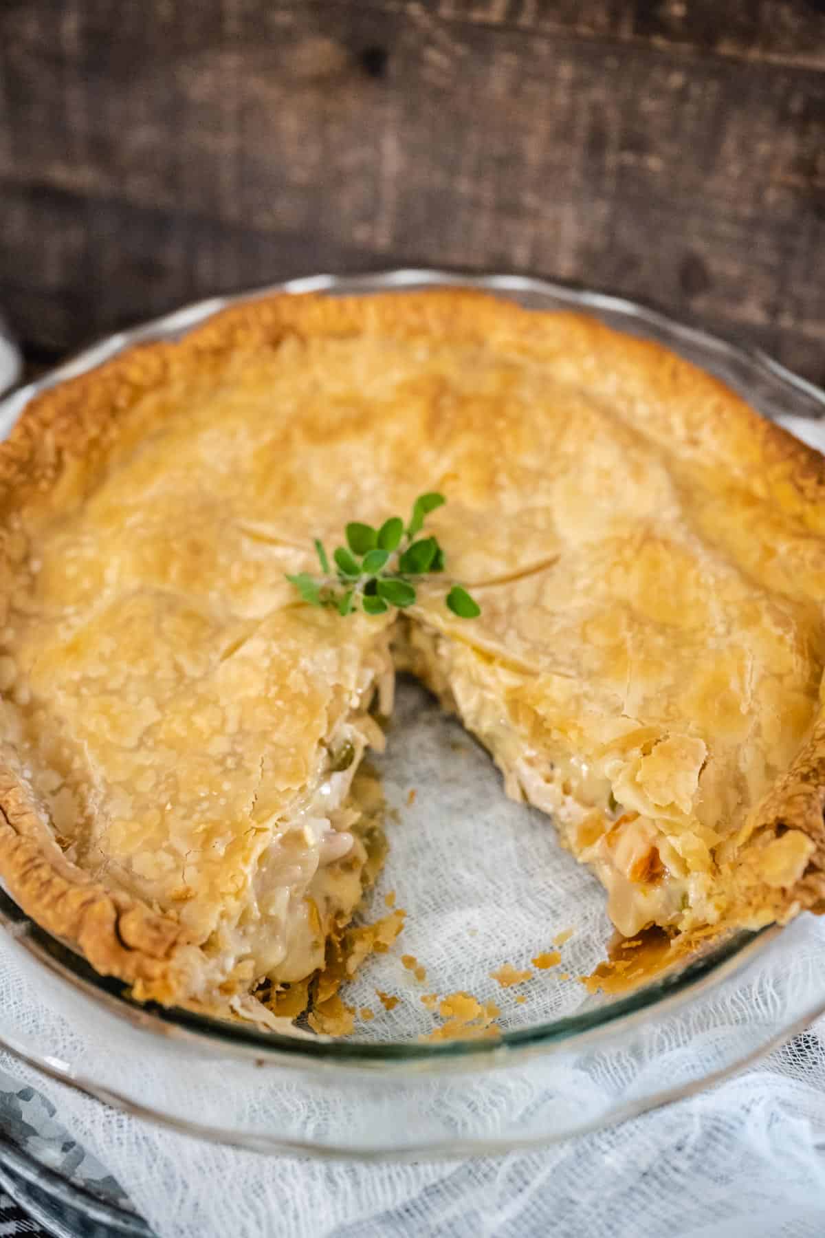 A chicken pot pie in a clear pie dish with one slice cut away from the whole pie.