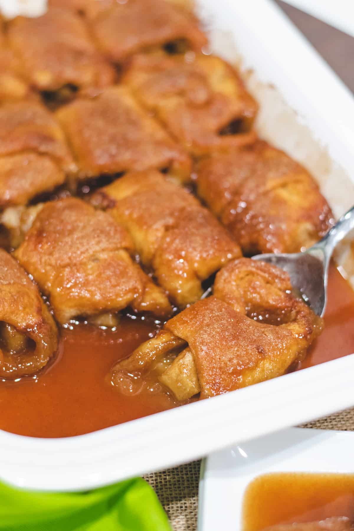 A white casserole dish with filled apple dumplings with a spoon scooping out an apple dumpling.