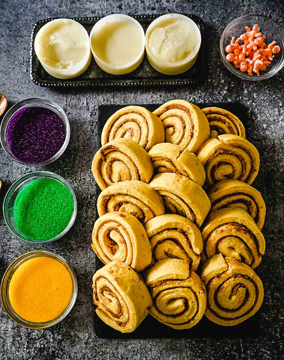 Image of easy king cake recipe ingredients: canned cinnamon rolls, icing, purple, green and yellow sugar, and toy babies.