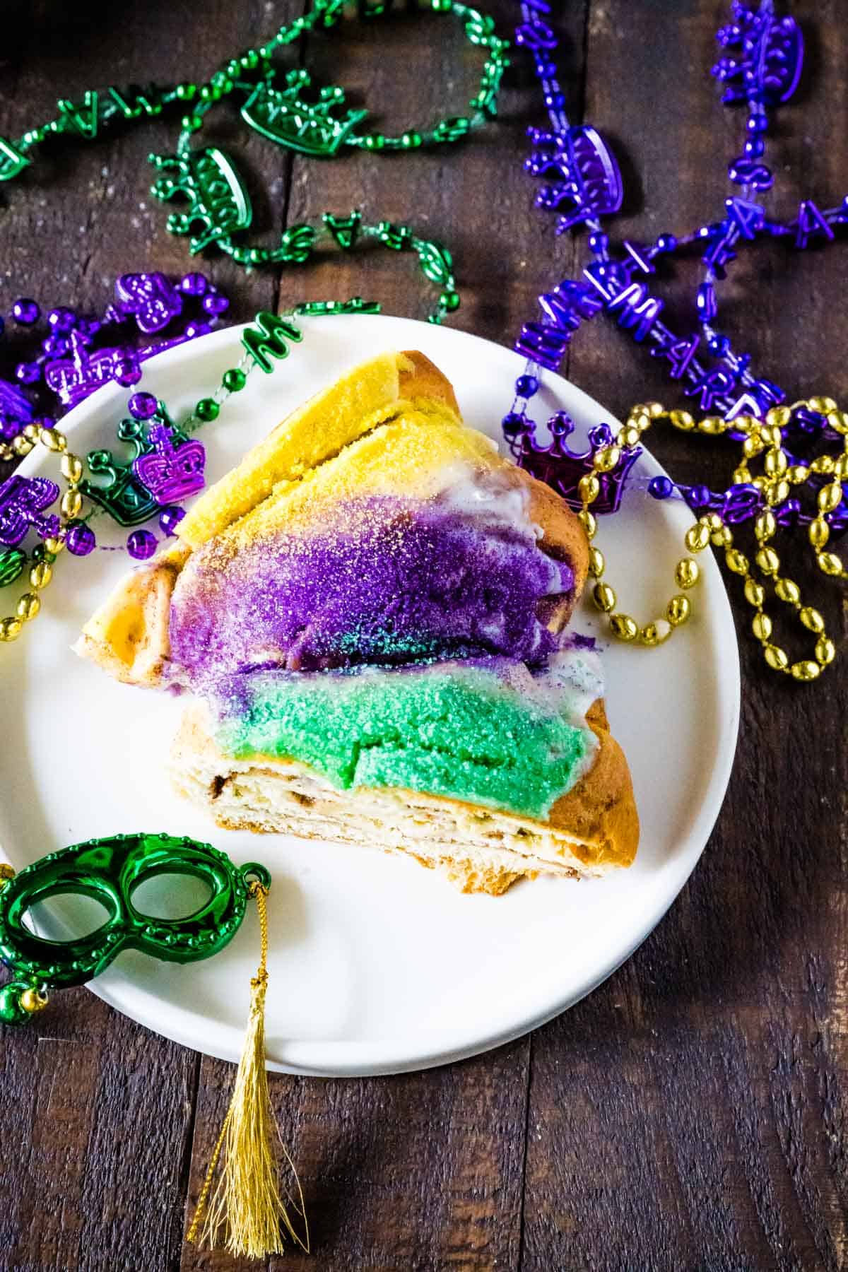 An overhead image of a slice of king cake topped with icing and yellow, green, and purple sugar.