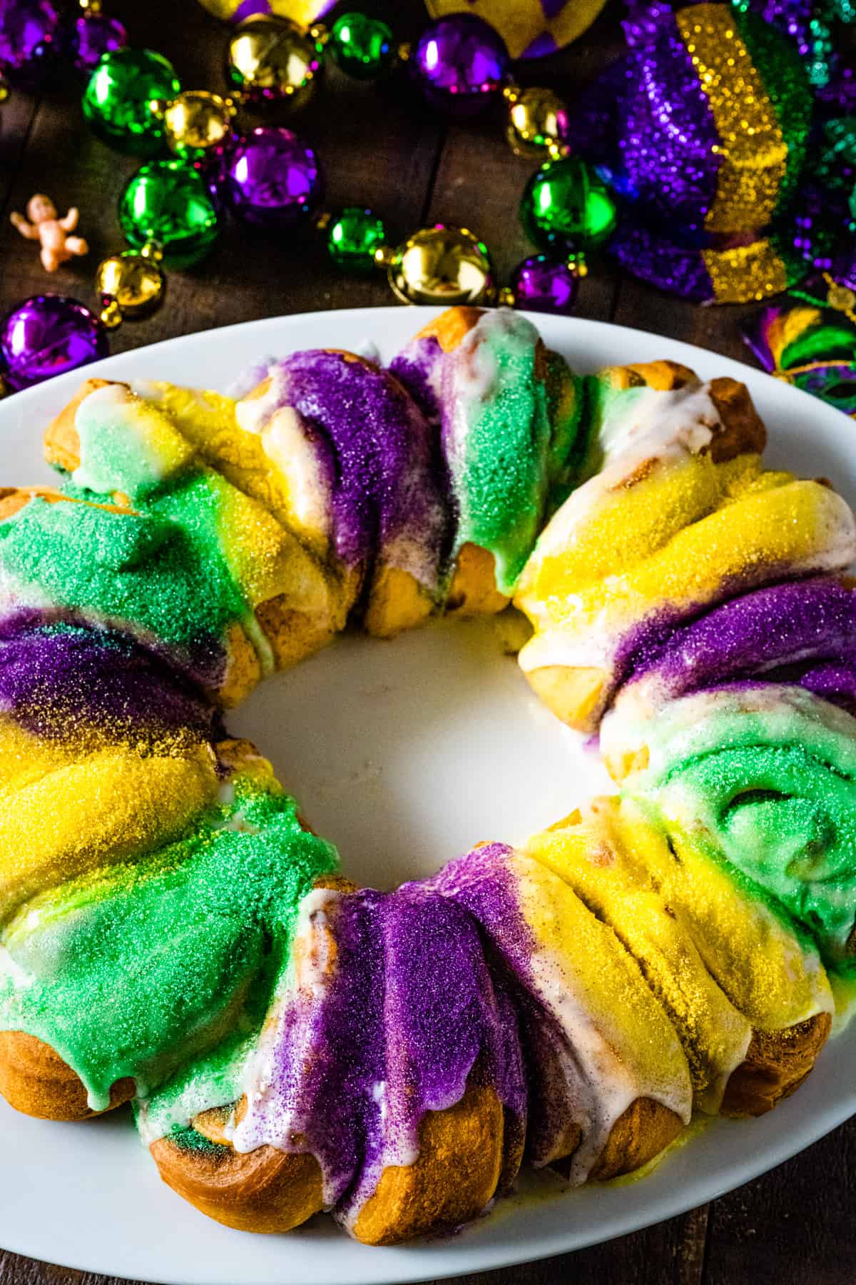 A whole easy king cake with mardi gras beads scattered about on the table.