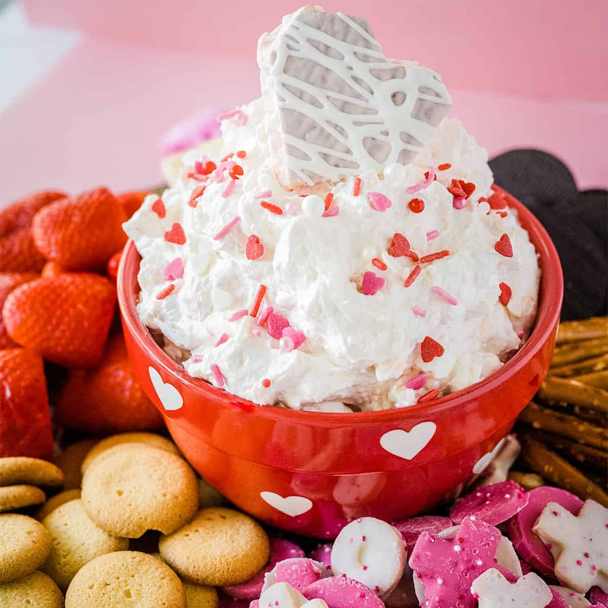 A red bowl of fluffy dip topped with Valentine's sprinkles and a little debbie heart snack cake on top.