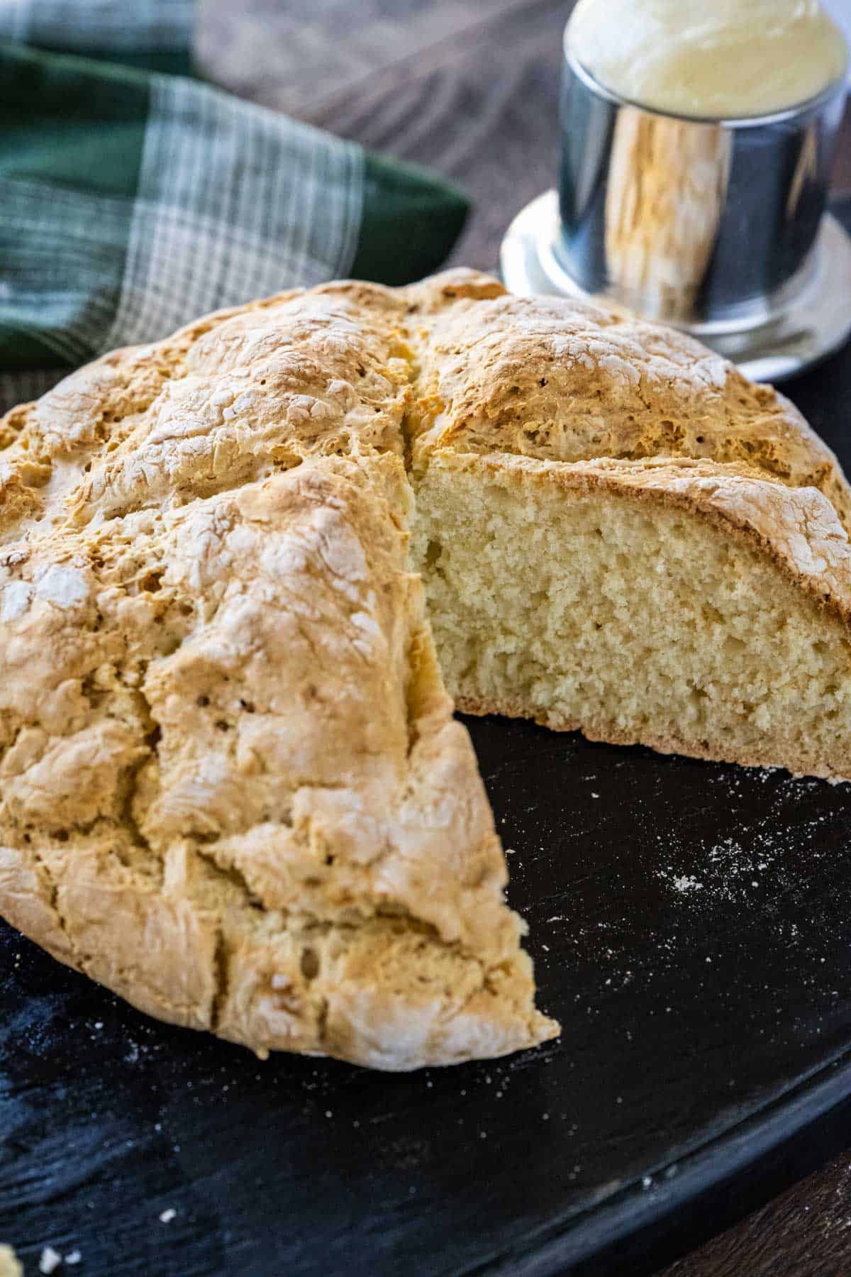 Irish soda bread with a slice removed on a serving board with fresh butter in a silver butter keeper in the background.