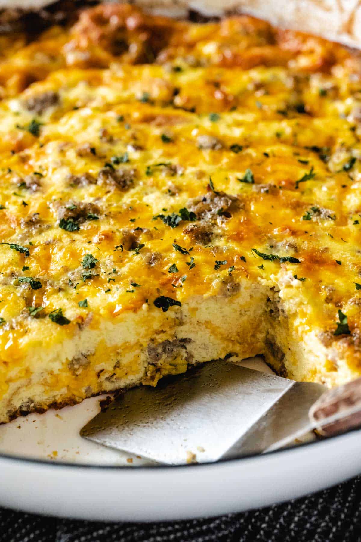 Upclose image of overnight breakfast casserole with a spatula removing a slice from the pan.