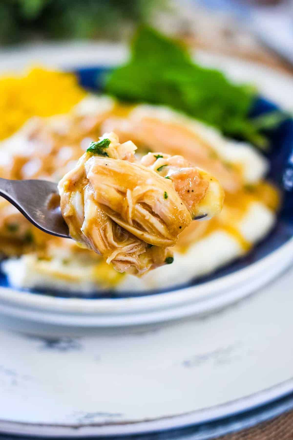 A fork full of chicken and gravy with the plated dish in the background.