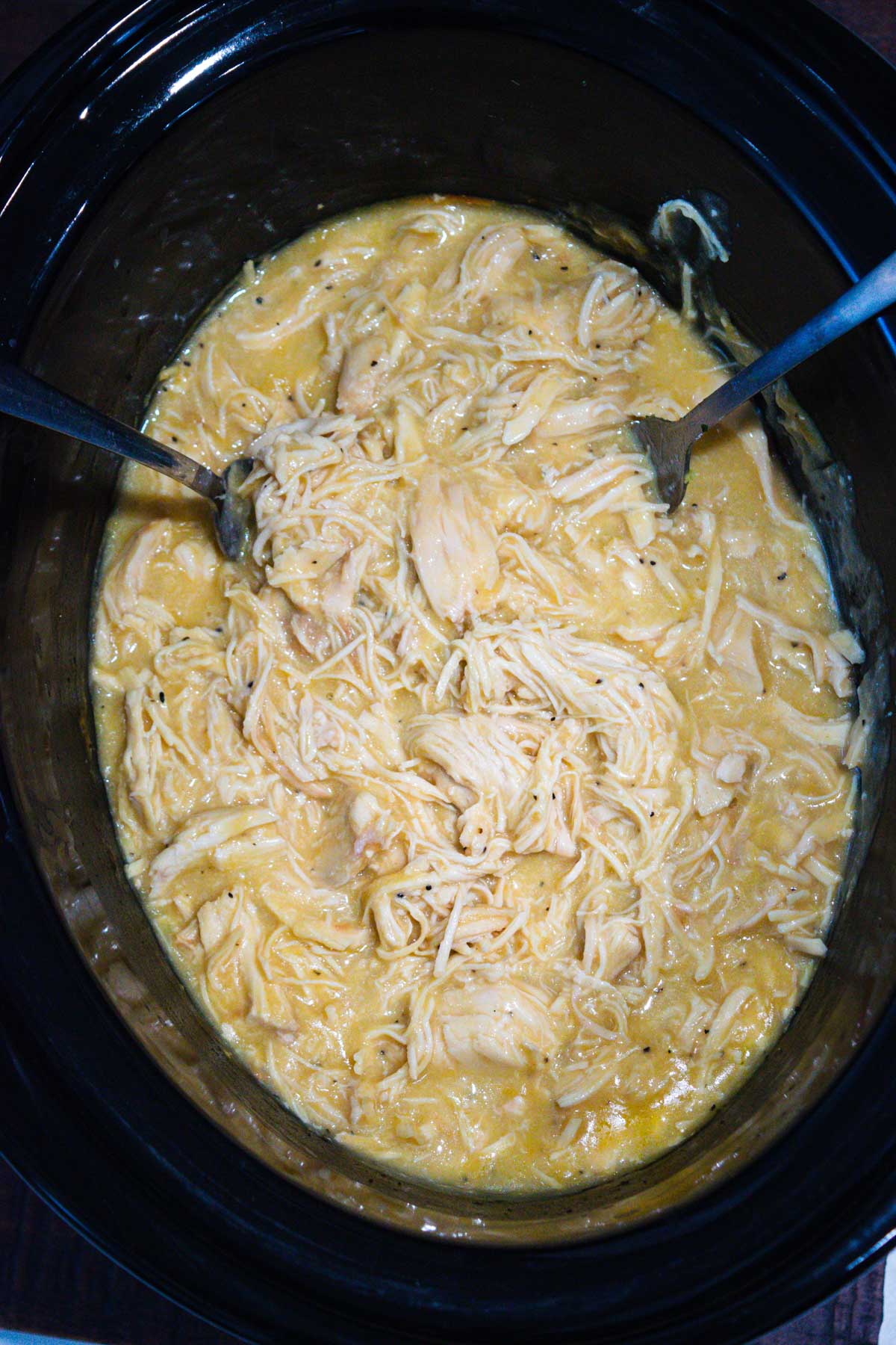 Overhead shot of chicken and gravy in the crock pot with two forks used to shred the chicken.