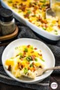 Image only of the Loaded mashed potatoes. Two dishes are on the table, one is a serving and the other is tha casserole dish.