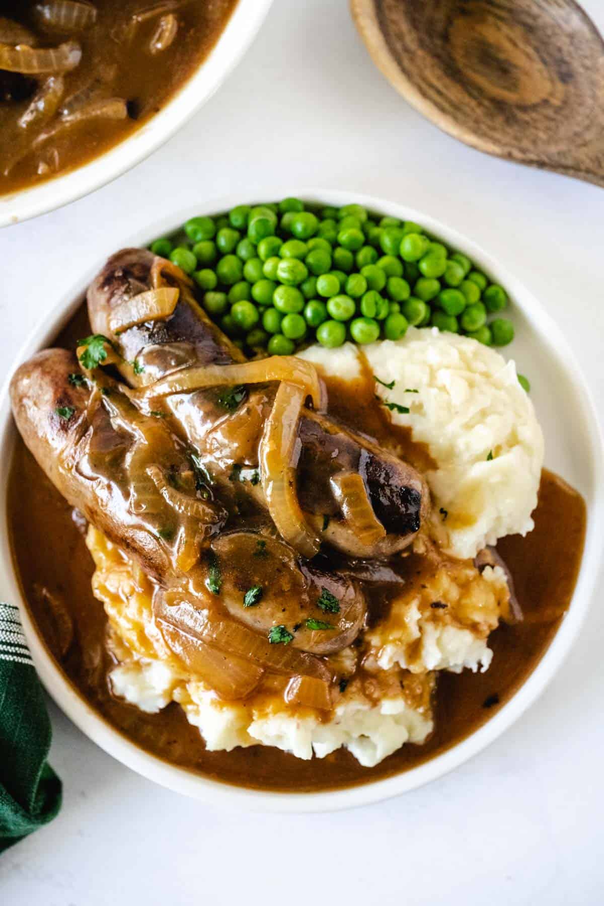 Bangers and mash plated with onion gravy and peas.