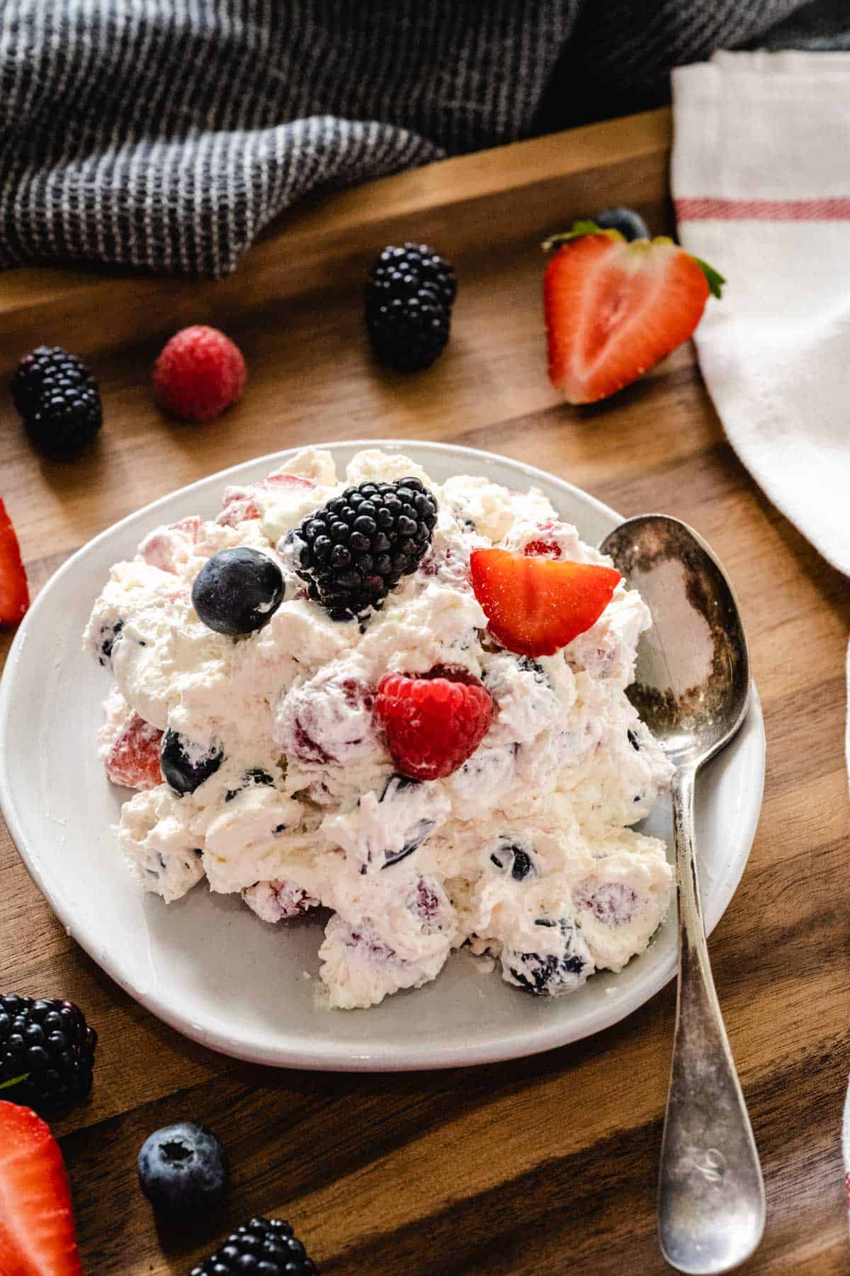 A plate full of summer berry cheesecake salad with a vintage spoon on the plate set on a wooden tray with berries.