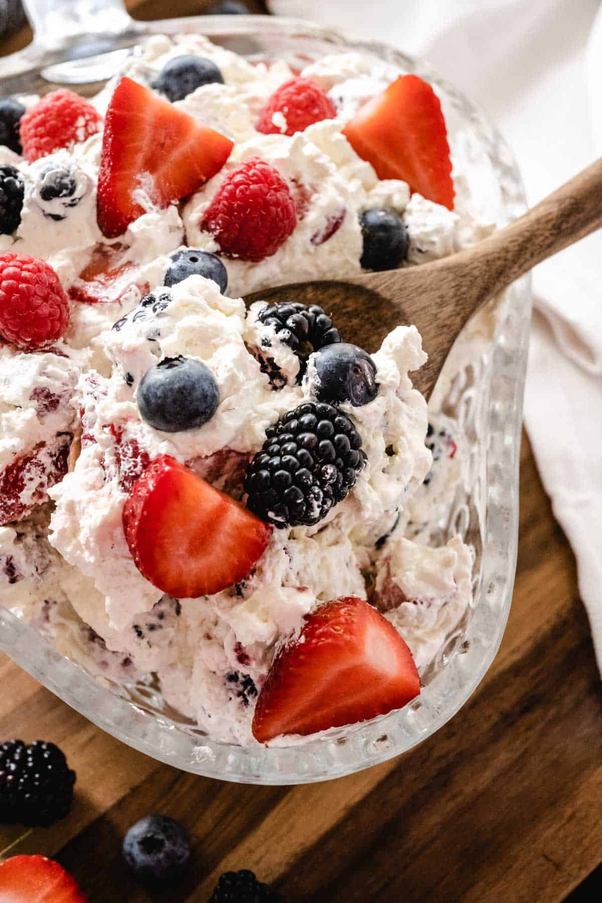 Berry cheesecake salad being spooned into a glass strawberry shaped serving dish.