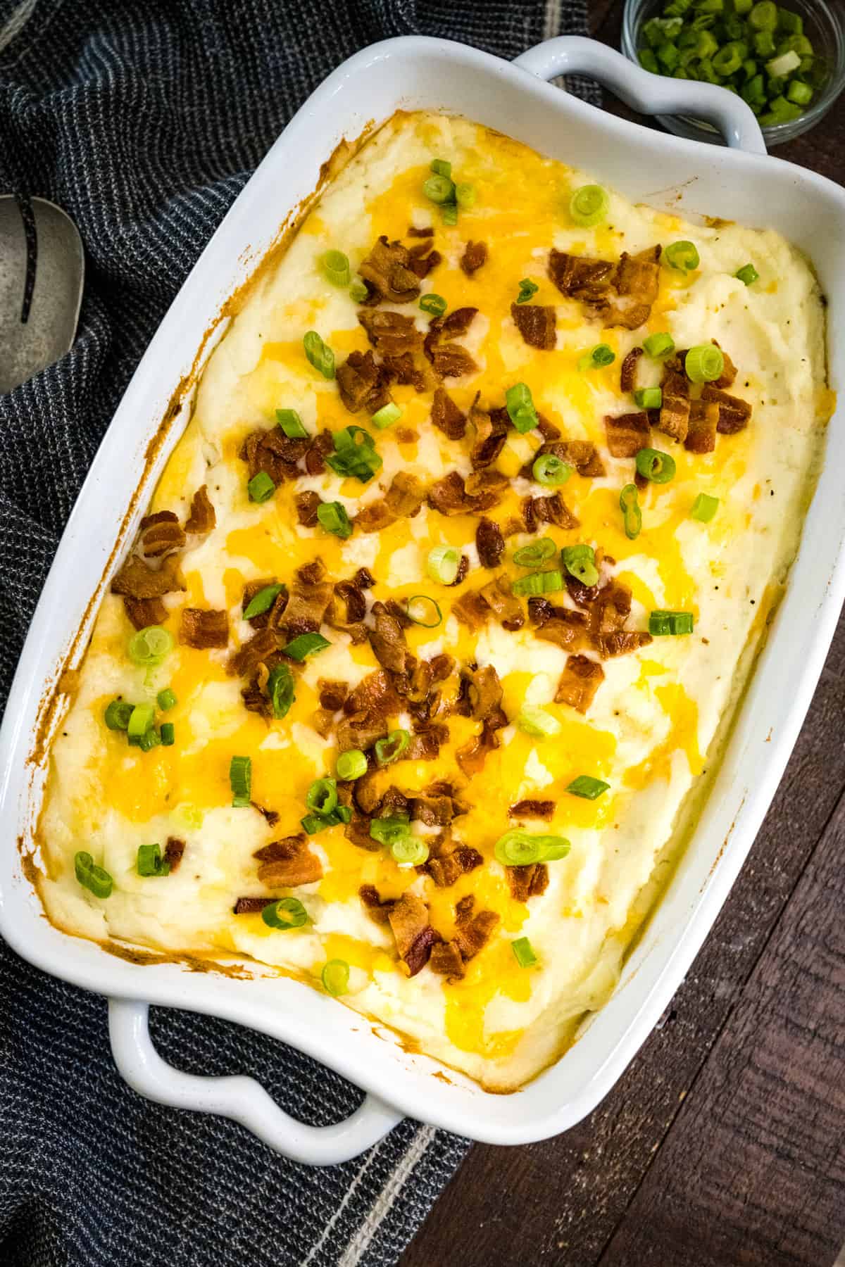 Casserole dish filled with baked loaded mashed potatoes topped with melted cheese, bacon and chives.