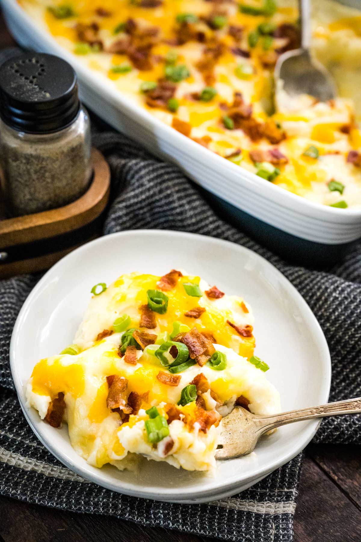 A plate full of creamy loaded mashed potatoes on a wooden table with pepper shaker in the background.