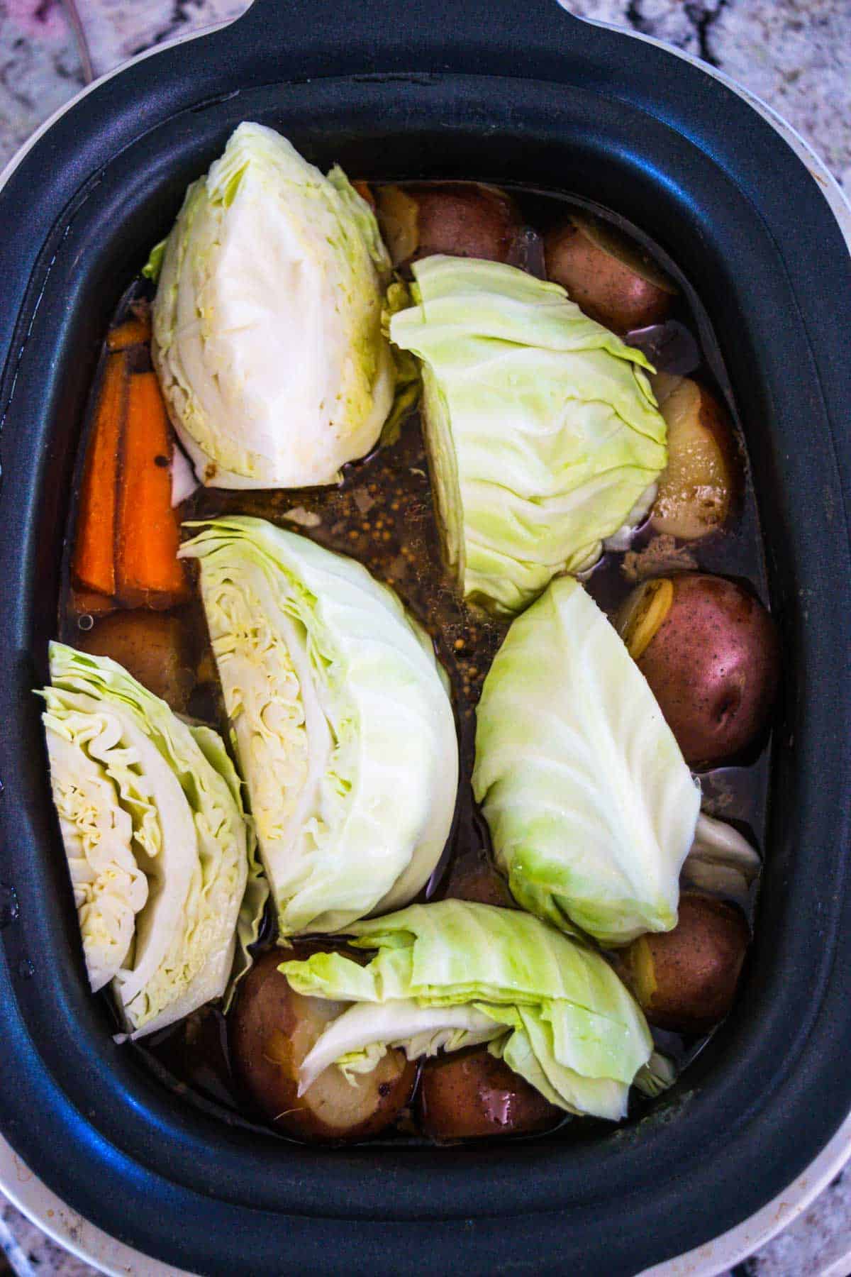 Slow cooker filled with corned beef, carrots, cabbage, and spices.