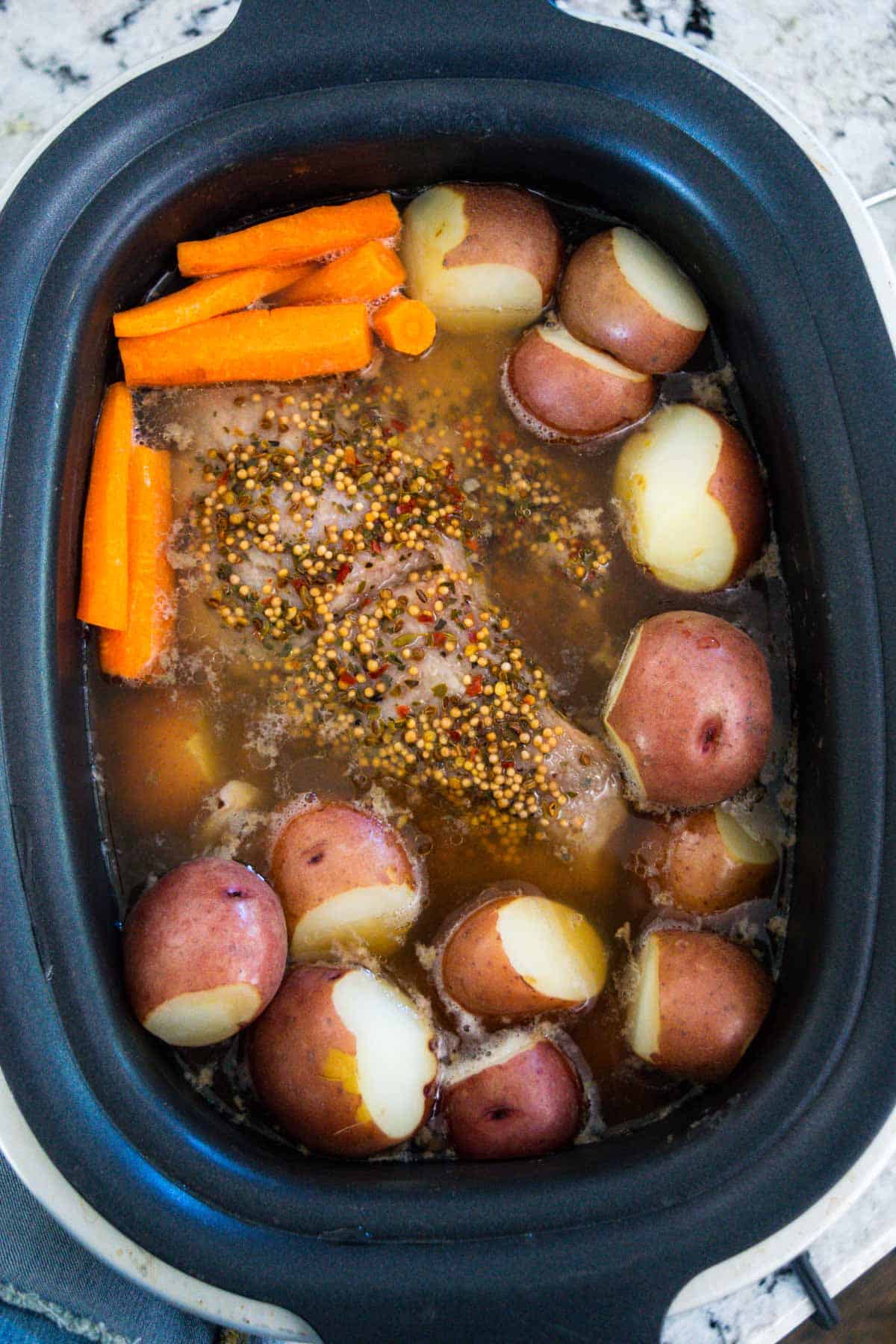 Slow cooker filled with corned beef, carrots, potatoes, and spices.