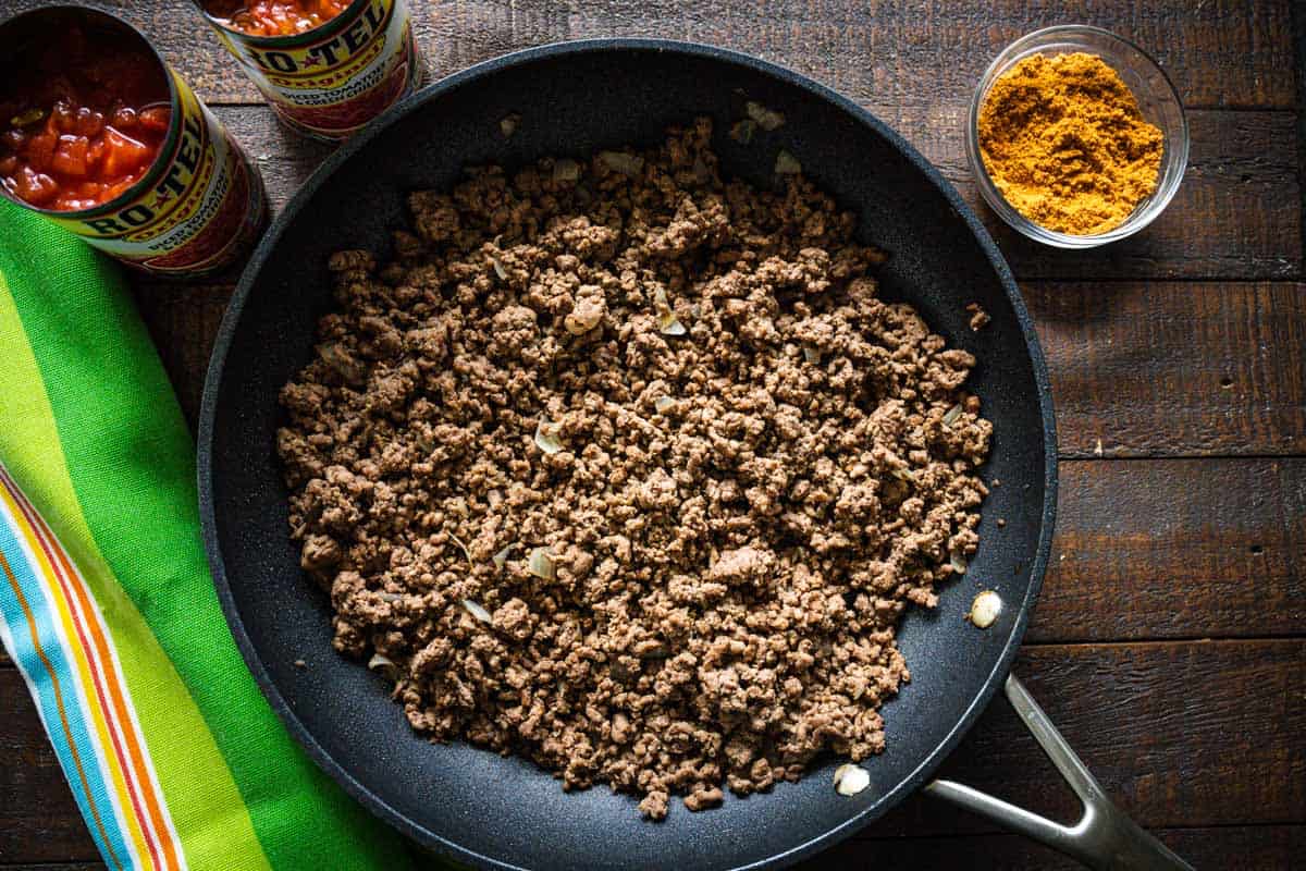 Cooked ground beef, onions, and garlic in a black skillet.