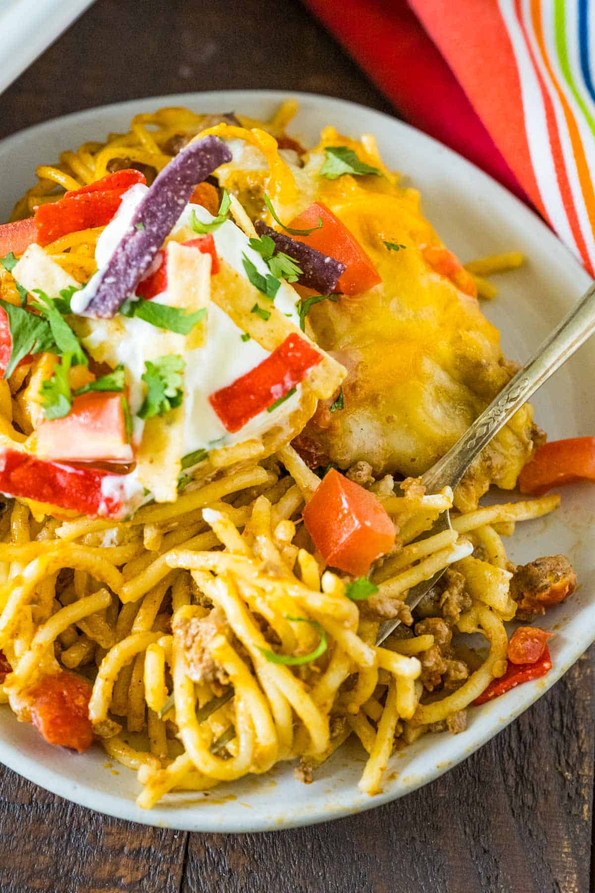 Taco spaghetti bake served on a rustic gray plate with a fork full of a bite ready to eat.