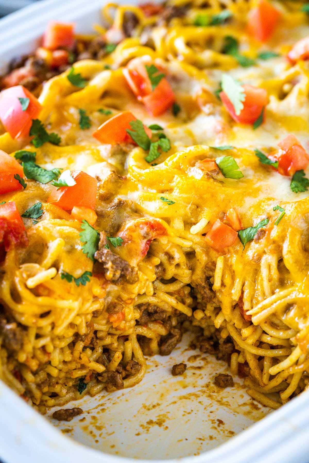 Taco spaghetti bake with a slic remove in a white casserole dish.