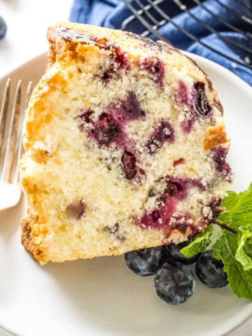 Up-close image of a slice of blueberry pound cake garnished with fresh blueberries and mint.