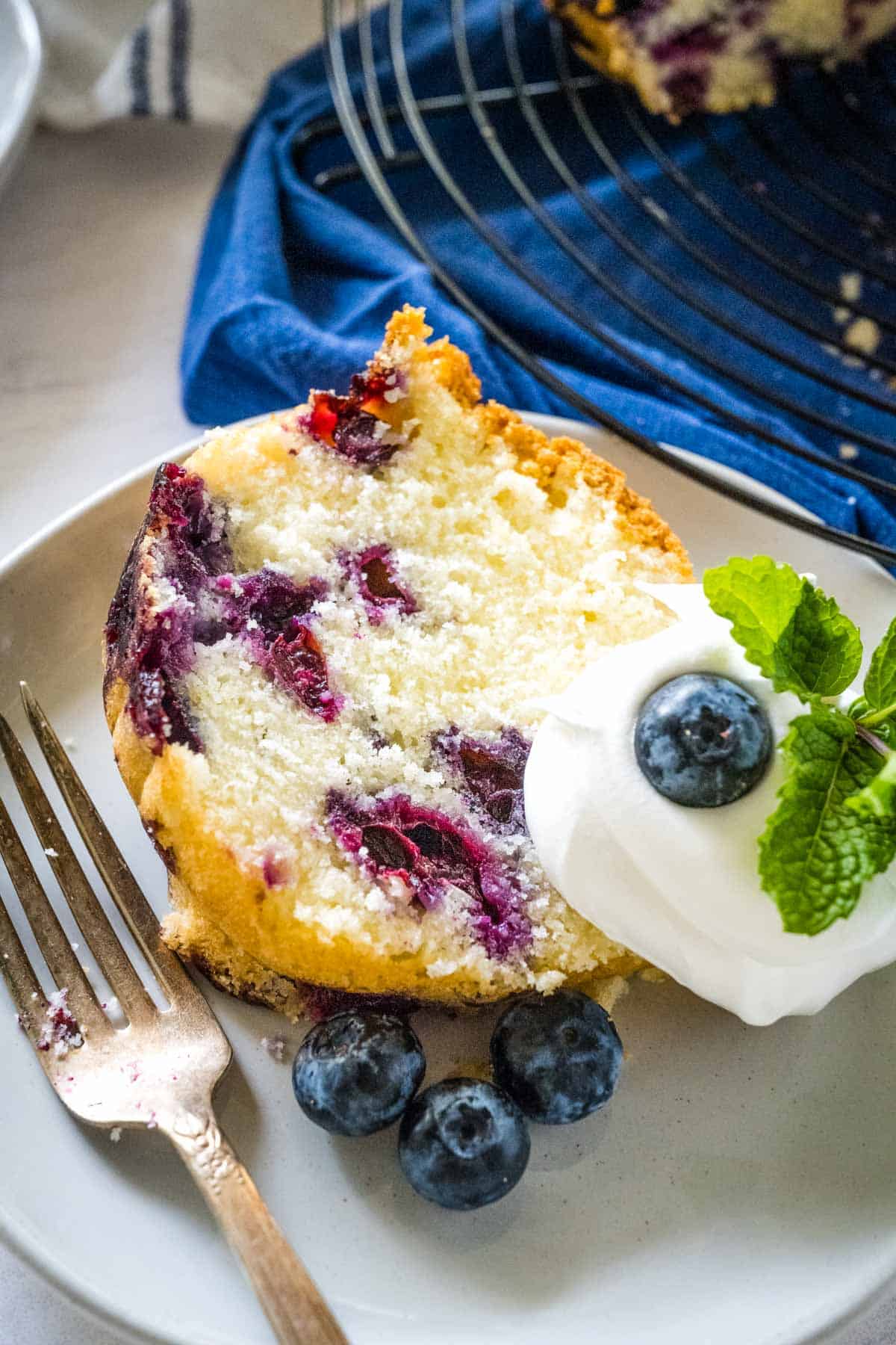 Slice of blueberry pound cake on a plate with a dollop of whipped cream.