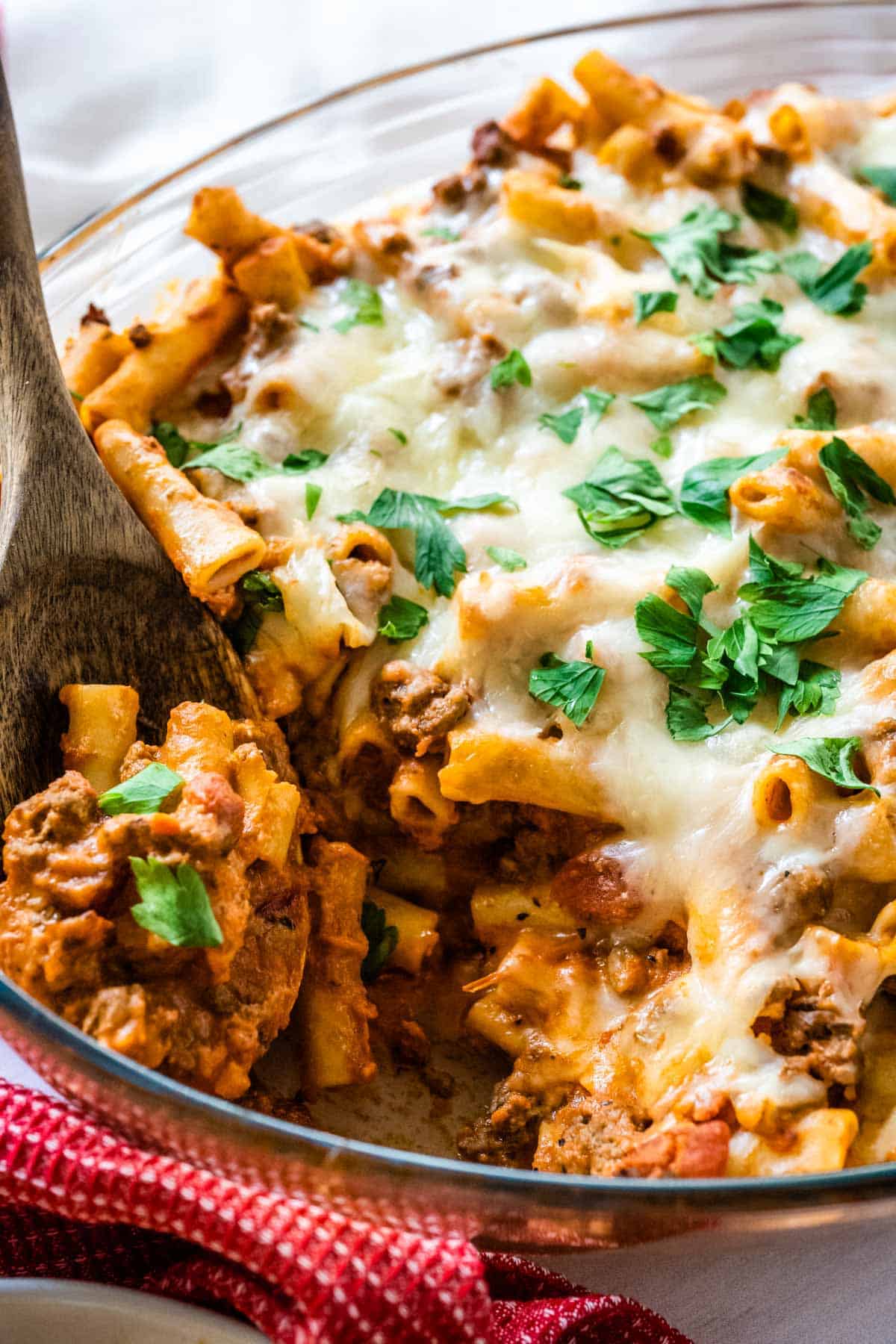 A spoon full of ziti with meat sauce being taken from a glass casserole dish.