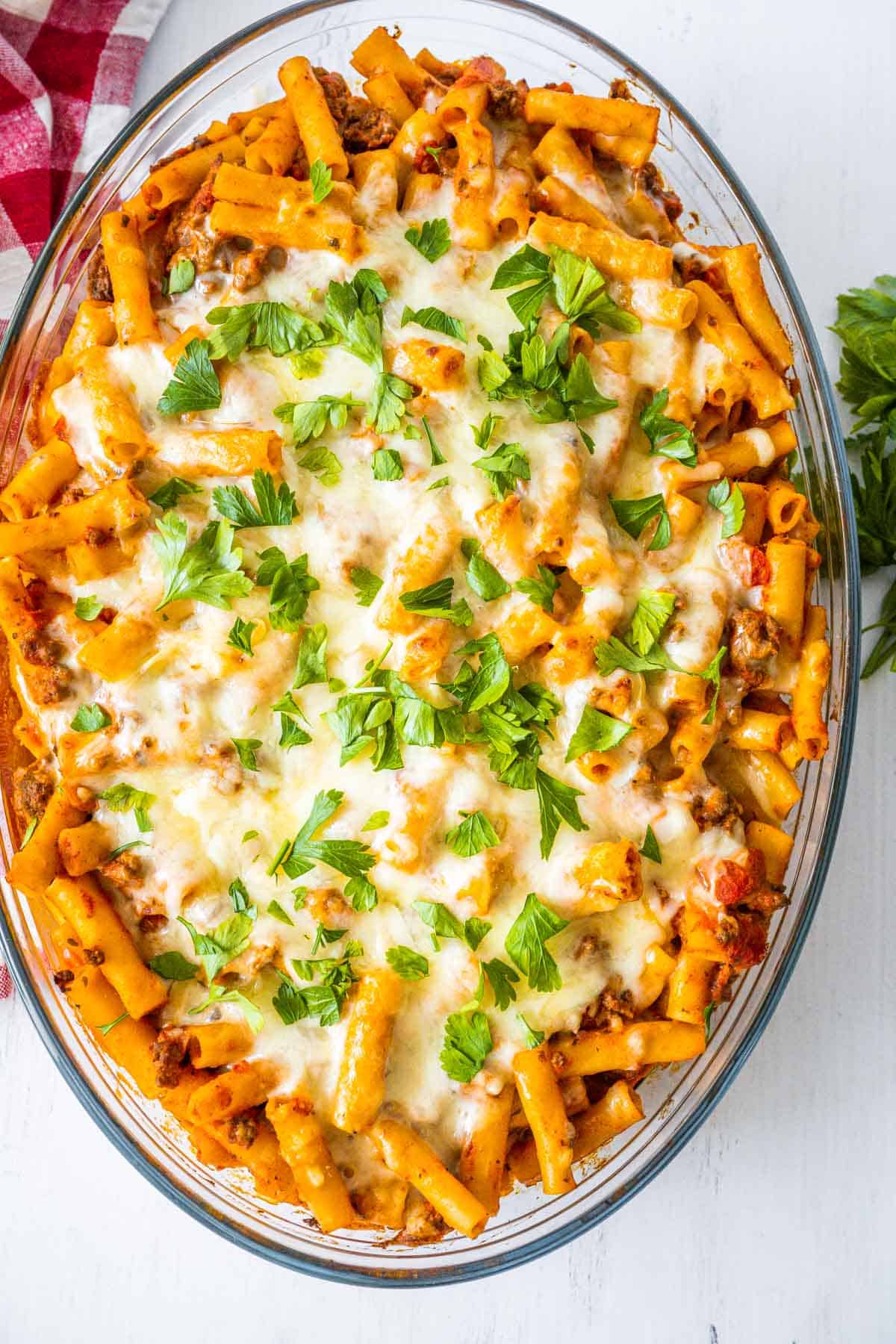 Overhead image of a clear casserole dish filled with baked ziti topped with mozzarella cheese and fresh parsley.