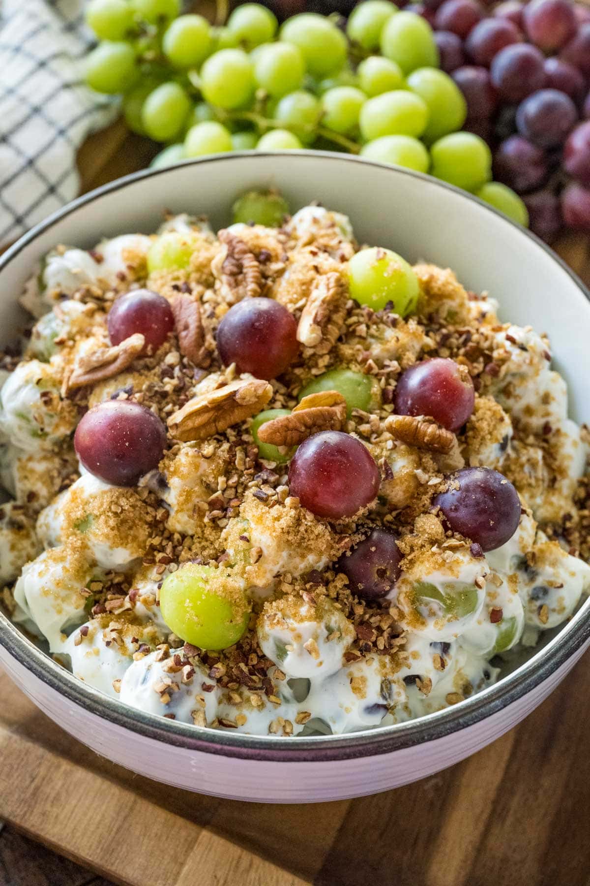 Creamy grape salad in a white bowl garnished with fresh grapes, pecans and crunchy brown sugar topping.