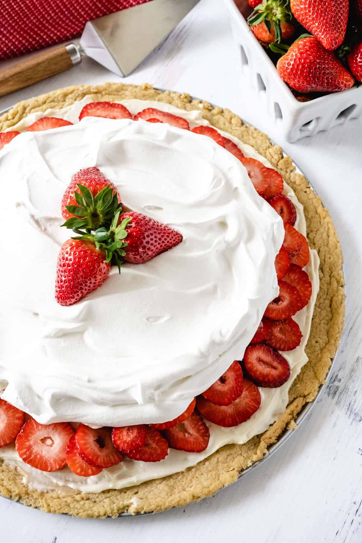 Up close image showing the layers of a whole strawberry dessert pizza garnished with three whole strawberries.